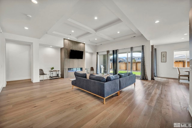 living room featuring beamed ceiling, a large fireplace, light wood-type flooring, and coffered ceiling