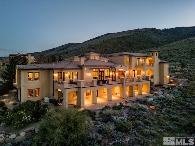 back house at dusk featuring a mountain view and a balcony