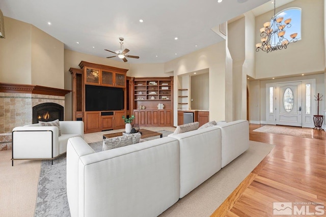 living room featuring a tile fireplace, built in shelves, ceiling fan with notable chandelier, and light hardwood / wood-style floors