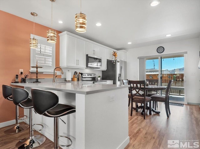 kitchen with white cabinetry, sink, stainless steel appliances, kitchen peninsula, and decorative light fixtures