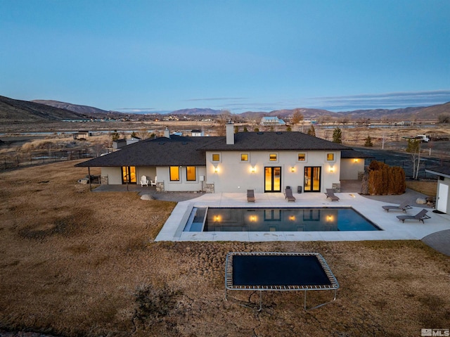 back house at dusk featuring a patio area, a mountain view, and a trampoline