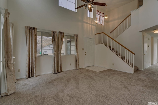 unfurnished living room featuring light carpet, ceiling fan with notable chandelier, and a high ceiling