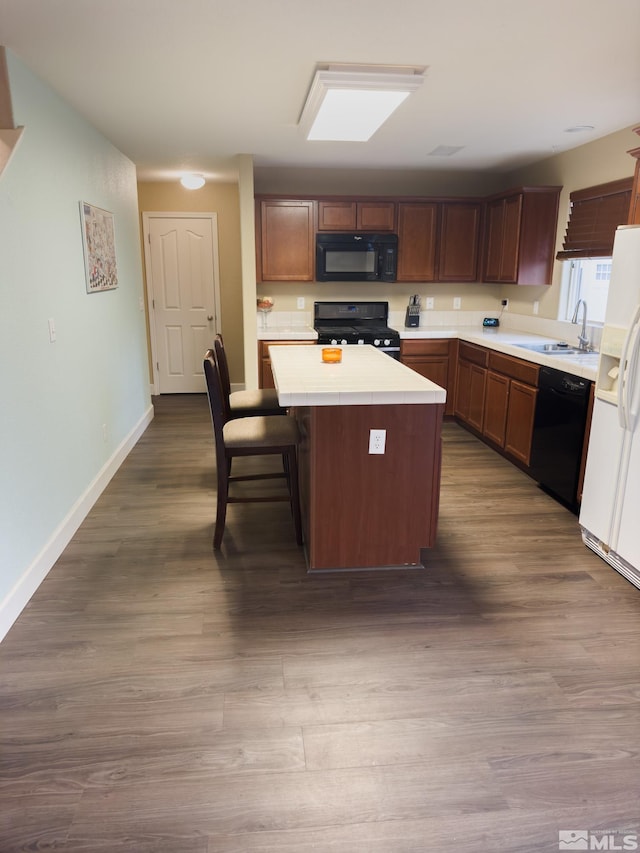 kitchen with a breakfast bar, black appliances, sink, hardwood / wood-style flooring, and a kitchen island