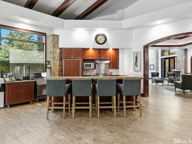 kitchen featuring a kitchen bar, a towering ceiling, a kitchen island with sink, and light hardwood / wood-style flooring