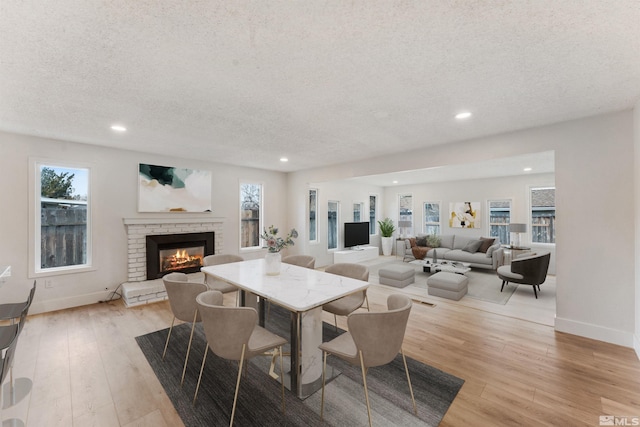 dining room featuring light hardwood / wood-style flooring, a textured ceiling, and a brick fireplace