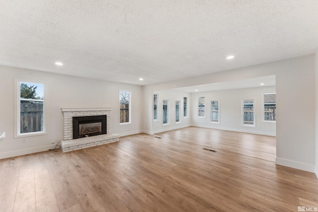 unfurnished living room with a fireplace, a textured ceiling, and light hardwood / wood-style flooring