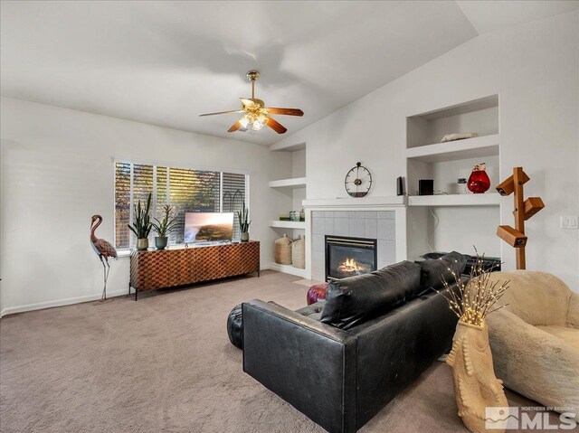 carpeted living room with built in shelves, ceiling fan, a tile fireplace, and lofted ceiling