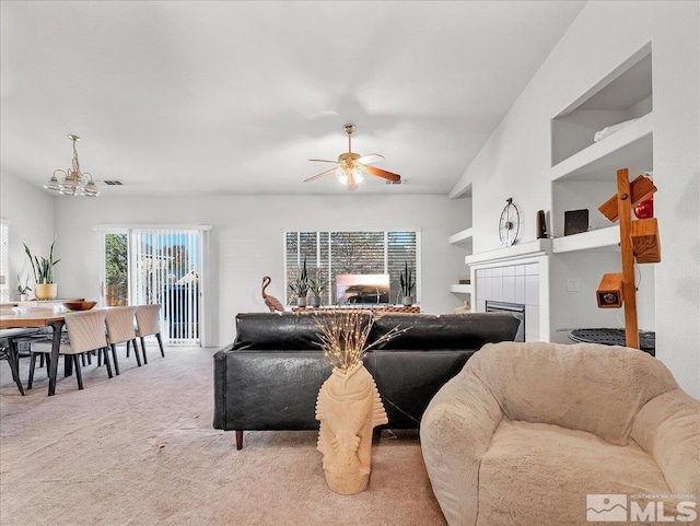 living room with carpet, ceiling fan, built in features, and a tiled fireplace