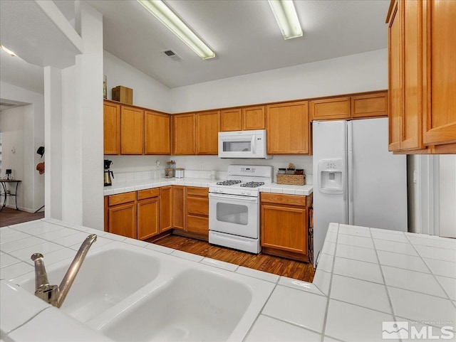 kitchen featuring white appliances, tile countertops, and lofted ceiling