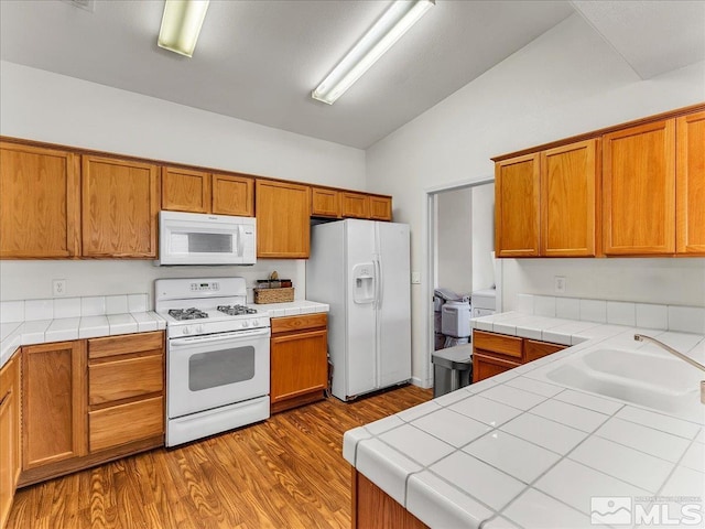 kitchen with tile countertops, lofted ceiling, white appliances, sink, and dark hardwood / wood-style flooring