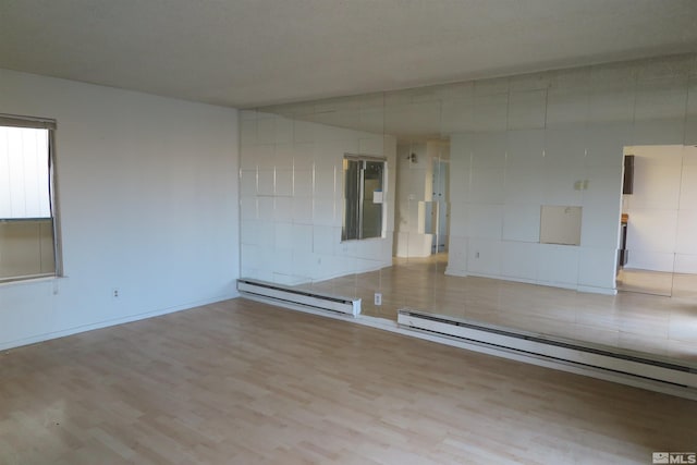 empty room with baseboard heating and light hardwood / wood-style flooring