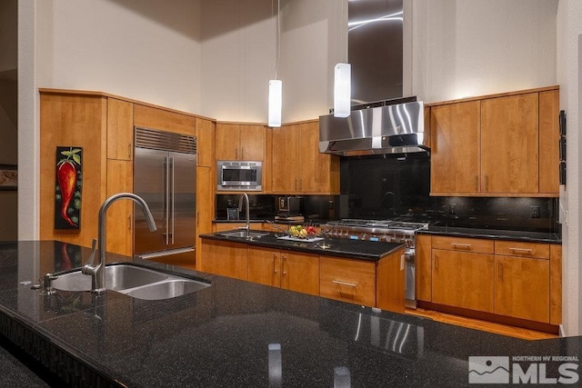 kitchen featuring a towering ceiling, sink, built in appliances, decorative light fixtures, and a center island with sink