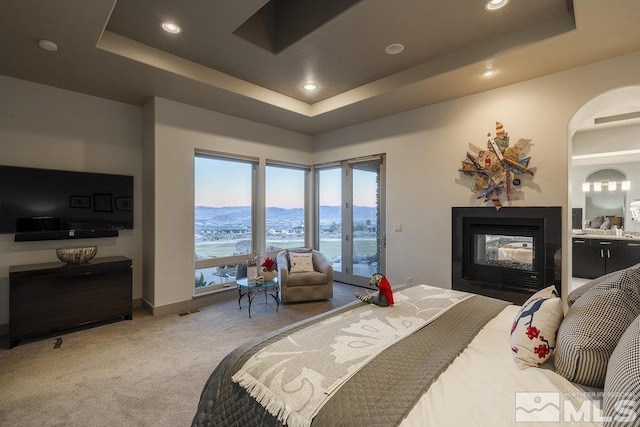 bedroom featuring a tray ceiling, a water view, carpet, and a multi sided fireplace