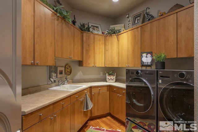 clothes washing area featuring separate washer and dryer, sink, cabinets, and light hardwood / wood-style flooring