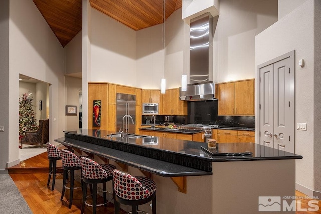 kitchen with a large island, high vaulted ceiling, wooden ceiling, and wall chimney range hood