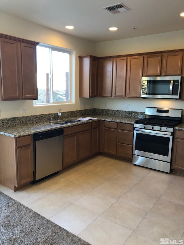 kitchen with appliances with stainless steel finishes, sink, light tile patterned floors, and dark stone countertops