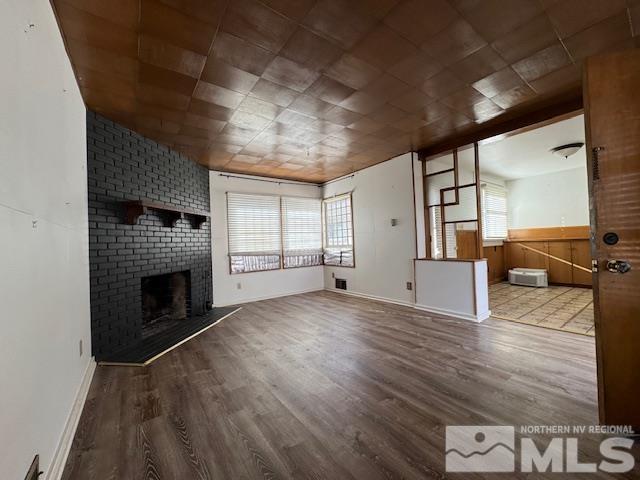 unfurnished living room with wood-type flooring and a brick fireplace