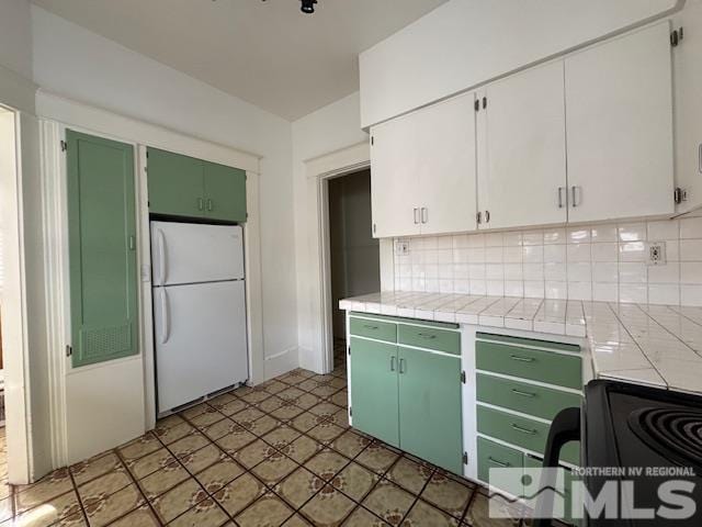 kitchen featuring tasteful backsplash, green cabinetry, white fridge, white cabinetry, and tile counters