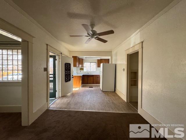 unfurnished living room with ceiling fan, crown molding, dark carpet, and a textured ceiling