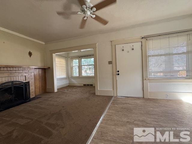 unfurnished living room with ceiling fan, a fireplace, dark carpet, and ornamental molding