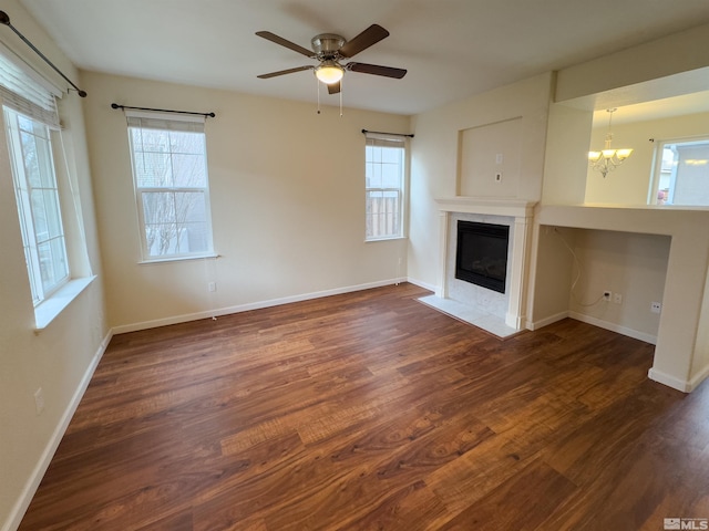 unfurnished living room featuring a healthy amount of sunlight, ceiling fan with notable chandelier, and dark wood-type flooring