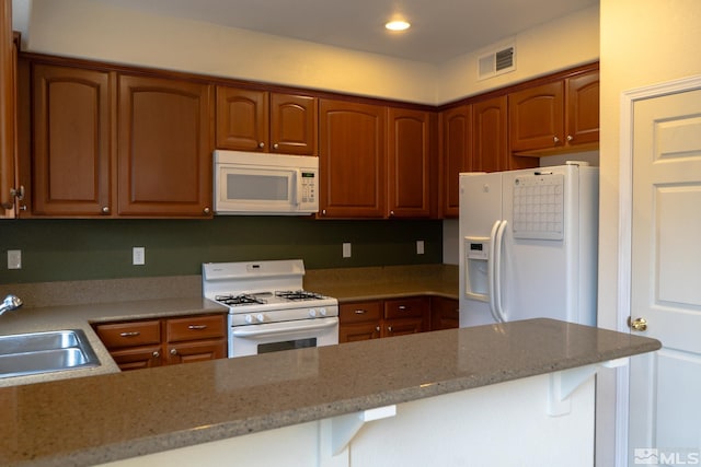 kitchen featuring light stone countertops, white appliances, kitchen peninsula, and sink