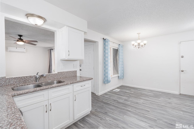 kitchen featuring sink, a wall mounted AC, a textured ceiling, white cabinets, and ceiling fan with notable chandelier