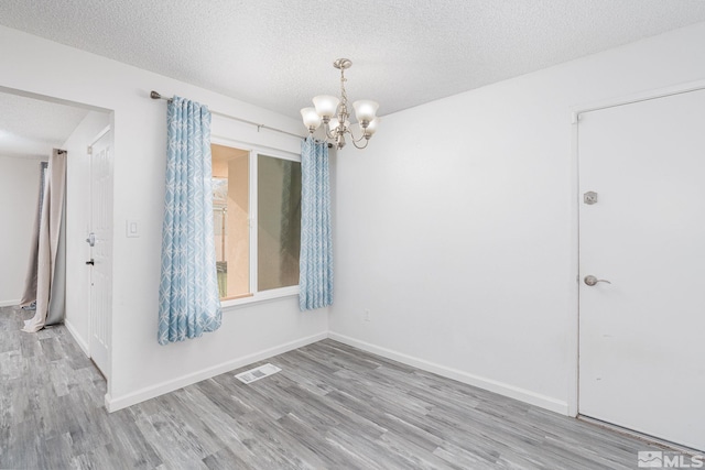 spare room featuring wood-type flooring, a textured ceiling, and an inviting chandelier