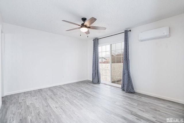 spare room with a textured ceiling, light hardwood / wood-style flooring, a wall unit AC, and ceiling fan