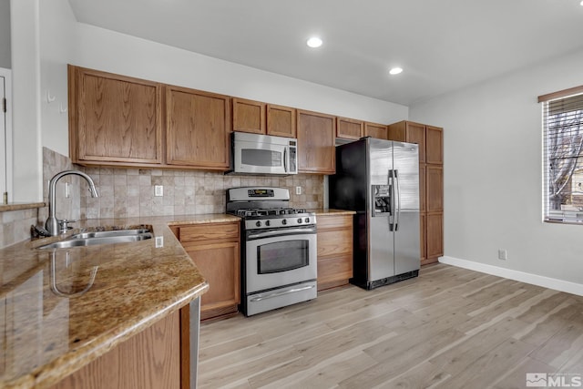 kitchen featuring light stone countertops, appliances with stainless steel finishes, backsplash, sink, and light hardwood / wood-style flooring