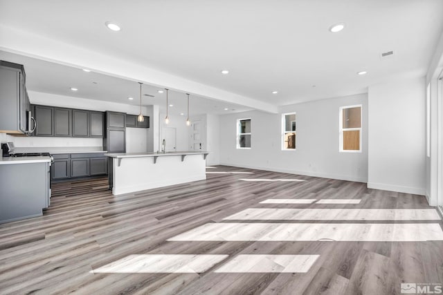 kitchen with light hardwood / wood-style flooring, hanging light fixtures, a center island with sink, gray cabinets, and stove