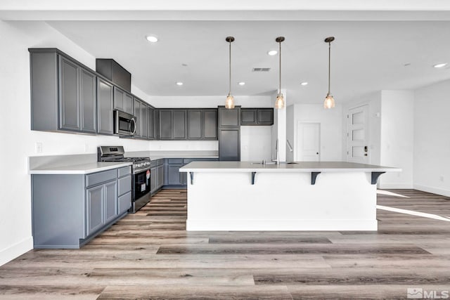 kitchen with pendant lighting, sink, appliances with stainless steel finishes, a kitchen island with sink, and light hardwood / wood-style floors