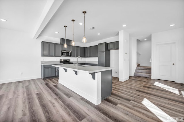 kitchen with gray cabinets, dark hardwood / wood-style floors, an island with sink, sink, and stainless steel appliances