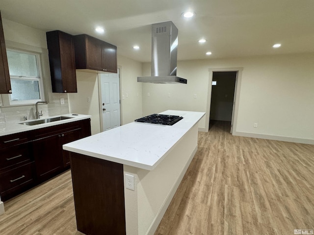 kitchen with ventilation hood, sink, gas stovetop, light hardwood / wood-style floors, and a kitchen island