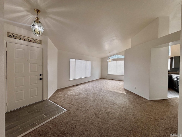 entryway with a chandelier, lofted ceiling, and dark carpet