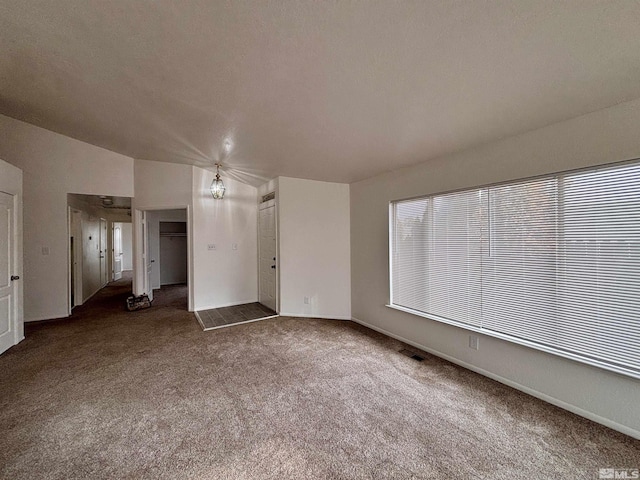 spare room with a notable chandelier and dark colored carpet