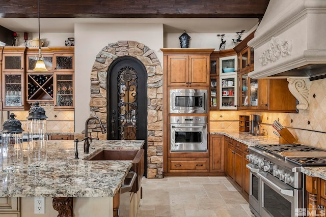 kitchen featuring appliances with stainless steel finishes, light stone counters, custom range hood, and sink