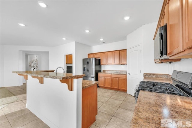 kitchen with light stone countertops, a kitchen island with sink, a breakfast bar, light tile patterned flooring, and black appliances