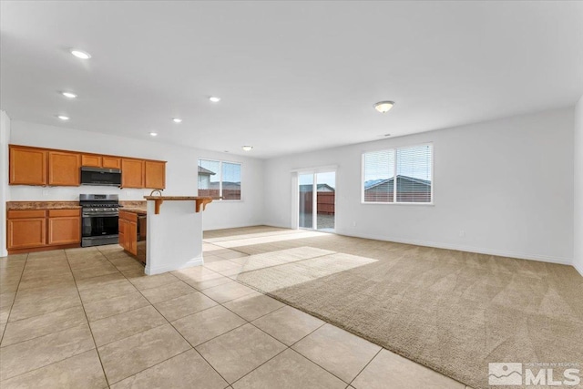 kitchen with a kitchen bar, light tile patterned floors, stainless steel appliances, and an island with sink