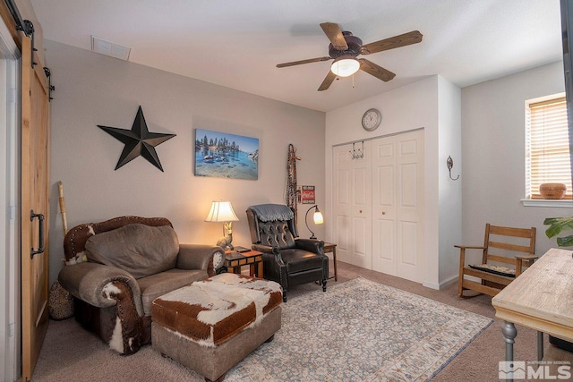 carpeted living room with ceiling fan and a barn door