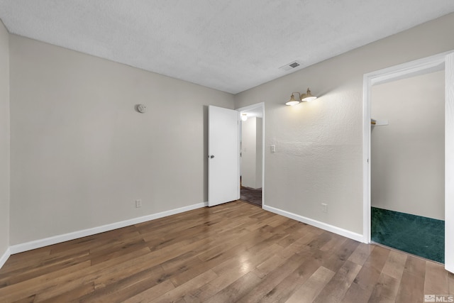 unfurnished bedroom with a walk in closet, wood-type flooring, and a textured ceiling