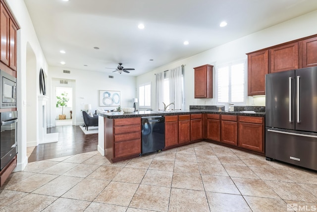 kitchen featuring ceiling fan, kitchen peninsula, dark stone counters, light tile patterned floors, and appliances with stainless steel finishes