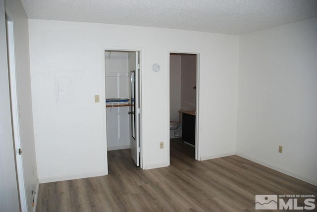 unfurnished bedroom with dark wood-type flooring, a textured ceiling, a closet, and a spacious closet