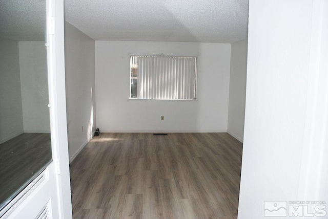 spare room featuring a textured ceiling and dark hardwood / wood-style flooring