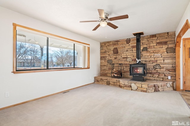 unfurnished living room featuring carpet, a wood stove, and ceiling fan