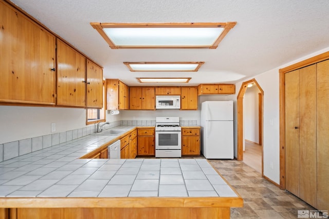 kitchen featuring kitchen peninsula, white appliances, tile counters, and sink