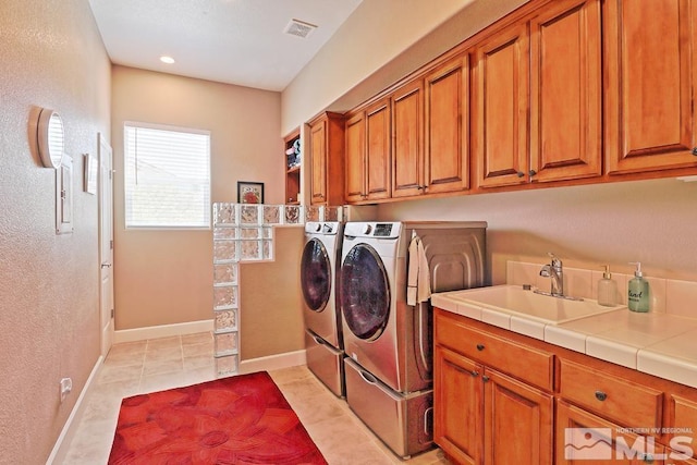 laundry area with washing machine and clothes dryer, sink, light tile patterned floors, and cabinets