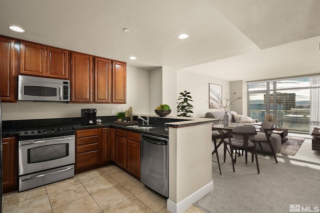 kitchen featuring kitchen peninsula, dark stone counters, stainless steel appliances, sink, and light tile patterned flooring