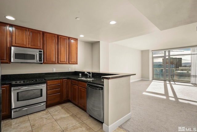 kitchen featuring sink, stainless steel appliances, kitchen peninsula, dark stone countertops, and light carpet