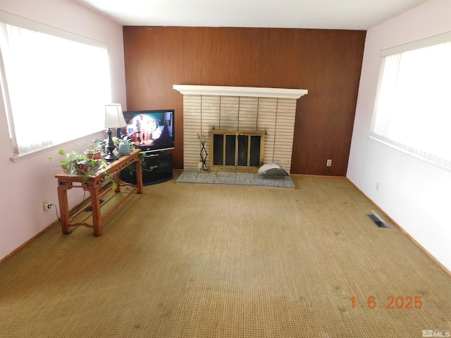 living room with light carpet, a healthy amount of sunlight, wood walls, and a brick fireplace